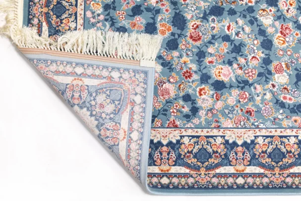 A Qaleen Carpets rug with a blue floral pattern and fringe, partially rolled up and against a white background