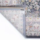 A Qaleen Carpets rug with a floral pattern and fringe, partially unrolled to show the underside and a label with a