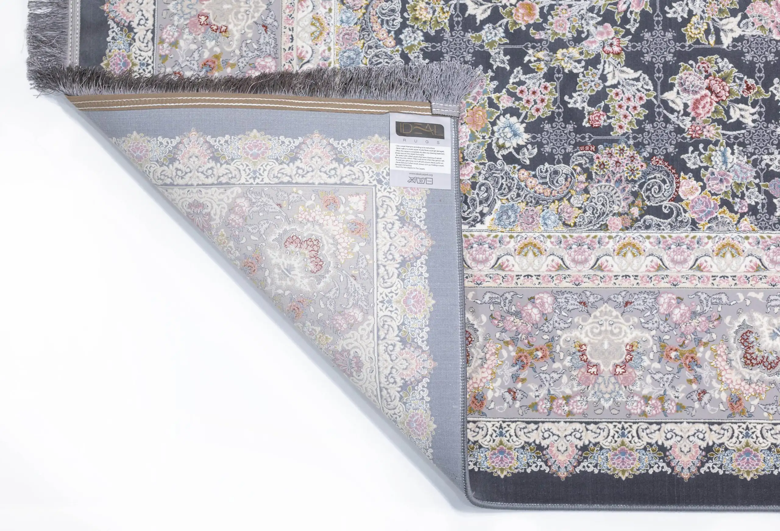 A Qaleen Carpets rug with a floral pattern and fringe, partially unrolled to show the underside and a label with a