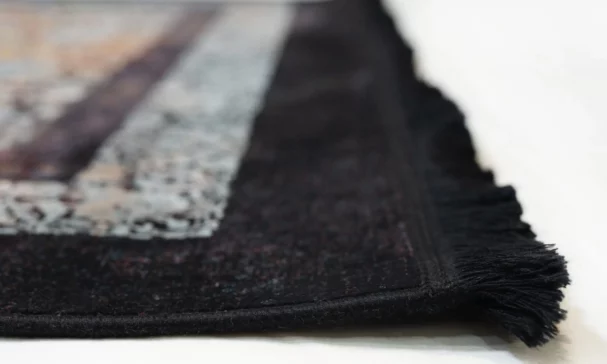 A close-up of a black and white rug with a fringe, made by Qaleen Carpets