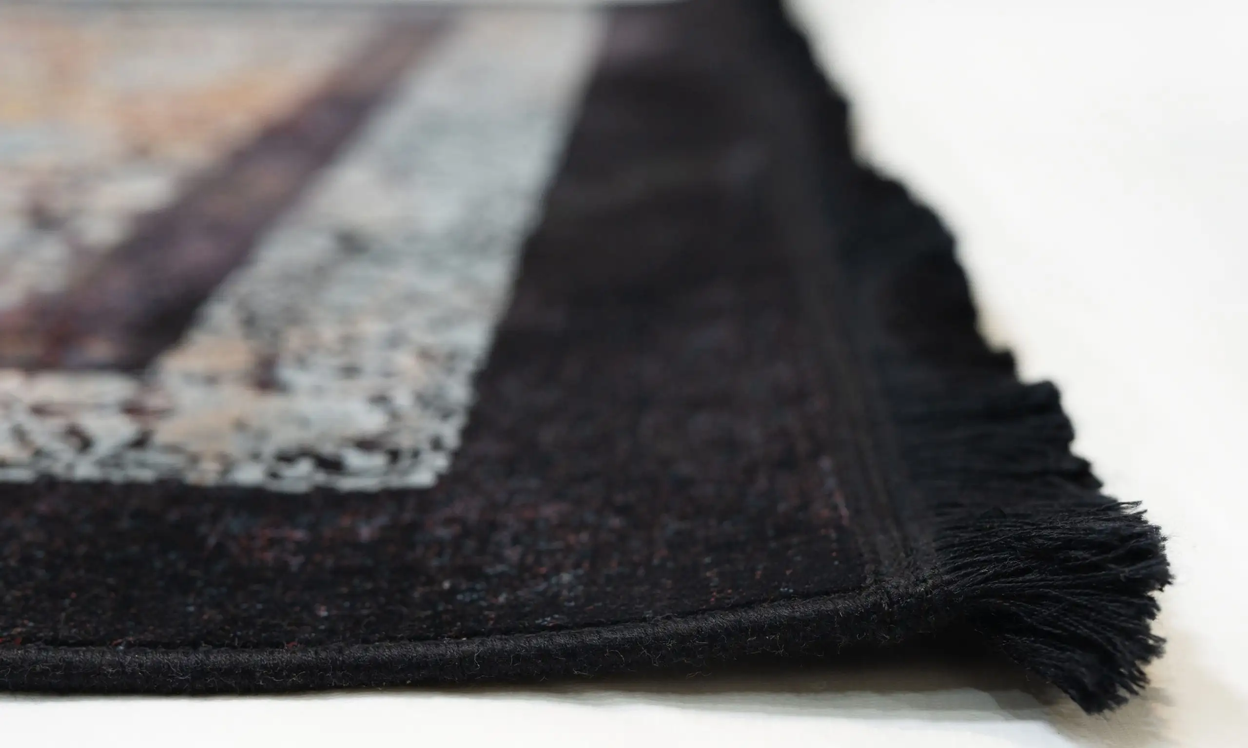 A close-up of a black and white rug with a fringe, made by Qaleen Carpets