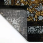 A close-up of a Qaleen Carpets rug with a gold and black floral pattern, partially unrolled and revealing its intricate