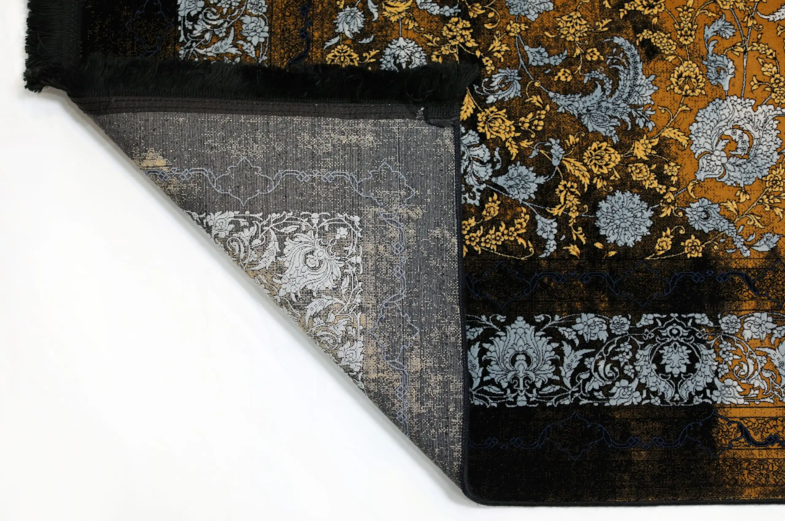 A close-up of a Qaleen Carpets rug with a gold and black floral pattern, partially unrolled and revealing its intricate