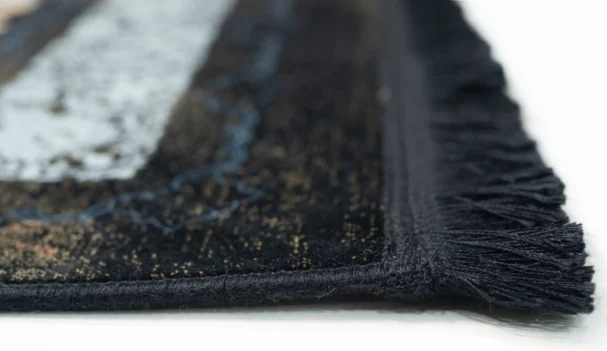 A close-up of a black and white rug with a fringe on a white background, made by Qaleen Carpets
