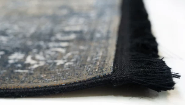 A close-up of a Qaleen Carpets rug with a fringe on a white surface, showcasing its intricate design and texture