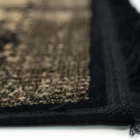 A close-up of a Qaleen Carpets rug with a black and gold pattern, featuring a fringe on one edge