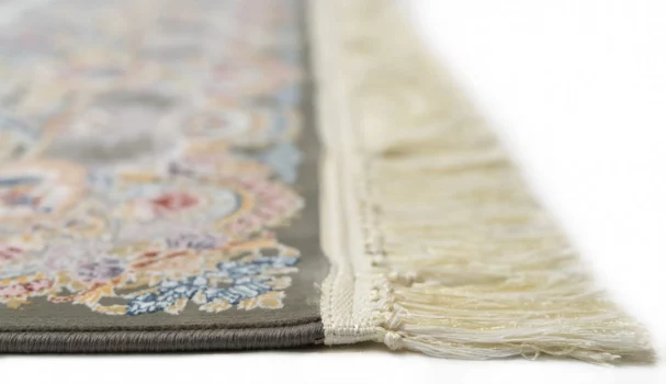 A close-up shot of a Qaleen Carpets rug, featuring a floral pattern on a gray background with a cream-colored fringe