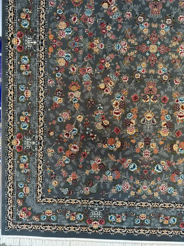 A close-up of a Qaleen Carpets rug with a floral pattern and a dark grey background, featuring a border and a fringe at the